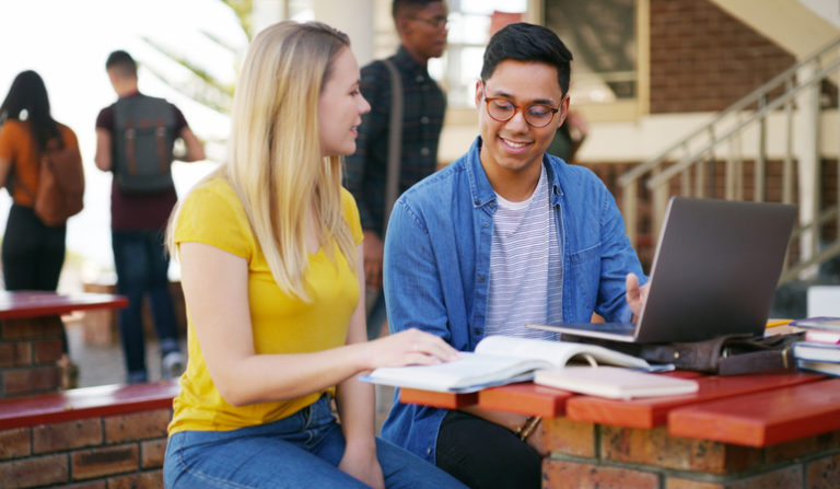 Cropped shot of two young students working on a laptop together while waiting for class outside of a school